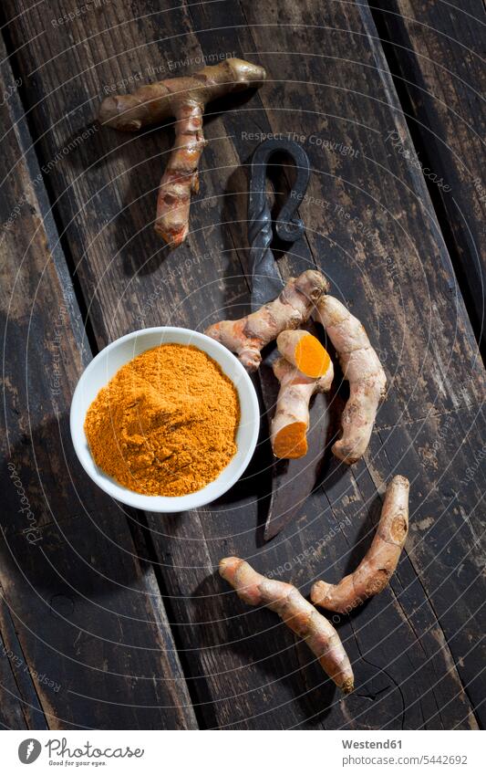 Whole and sliced turmeric, bowl of curcuma and an old knife on dark wood uncooked healthy eating nutrition overhead view from above top view Overhead