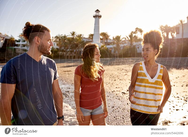 Spain, Canary Islands, Gran Canaria, three friends strolling on the beach at evening twilight beaches friendship in the evening looking eyeing enjoying
