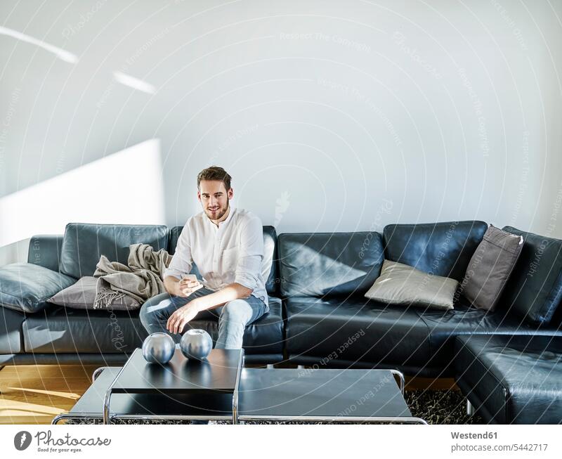 Smiling man sitting on couch holding cell phone smiling smile settee sofa sofas couches settees mobile phone mobiles mobile phones Cellphone cell phones Seated