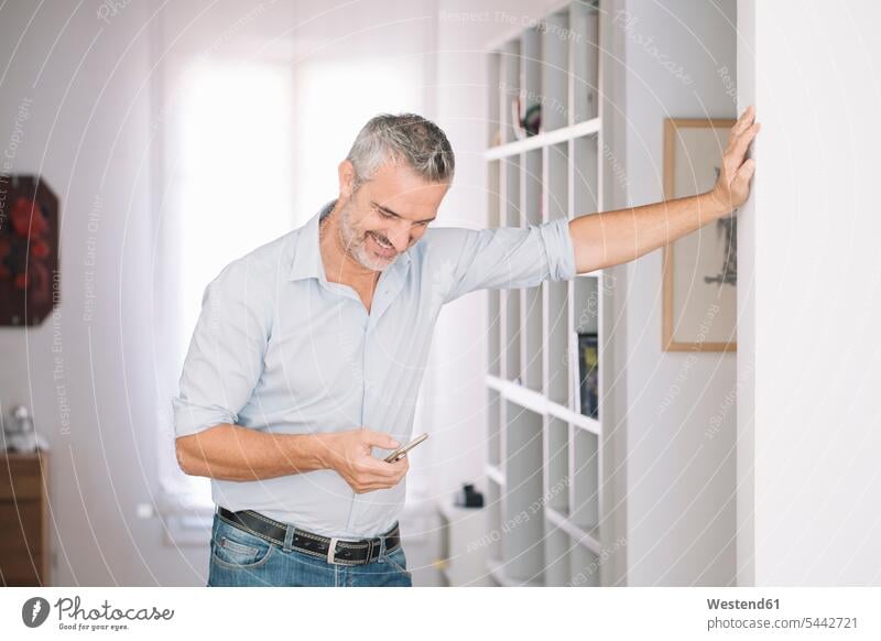 Smiling mature man using cell phone at home smiling smile men males mobile phone mobiles mobile phones Cellphone cell phones use Adults grown-ups grownups adult