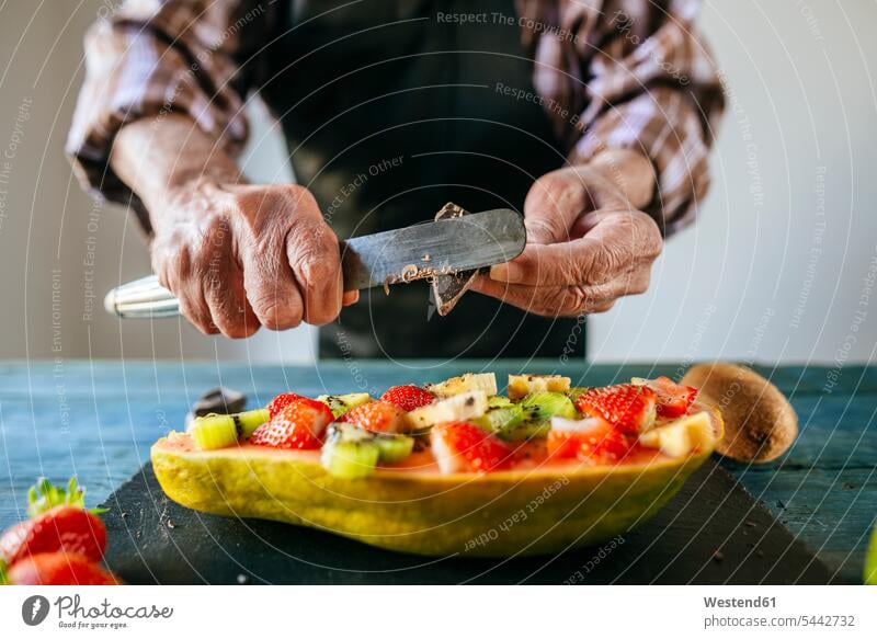 Close-up of man's hands cutting chocolate over half papaya with banana, kiwi and strawberries Papaya Pawpaw Papayas Pawpaws men males preparation prepare