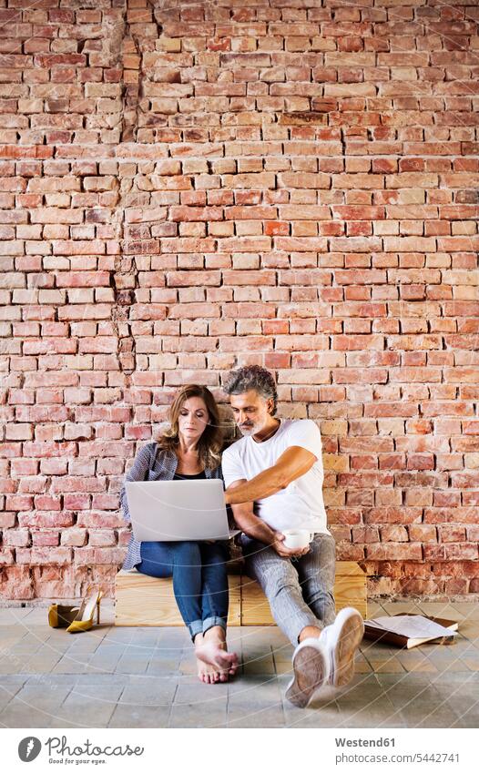 Businessman and woman sitting in a loft, using laptop, founding a start-up company Laptop Computers laptops notebook business people businesspeople startup