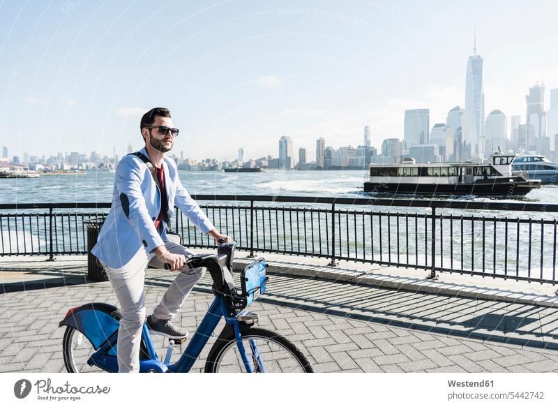 USA, man on bicycle at New Jersey waterfront with view to Manhattan Businessman Business man Businessmen Business men New York State driving drive bikes
