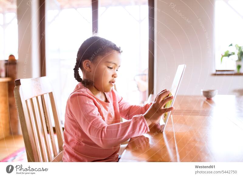 Little girl using sitting tablet, sitting at table Table Tables females girls alone solitary solo home at home digitizer Tablet Computer Tablet PC