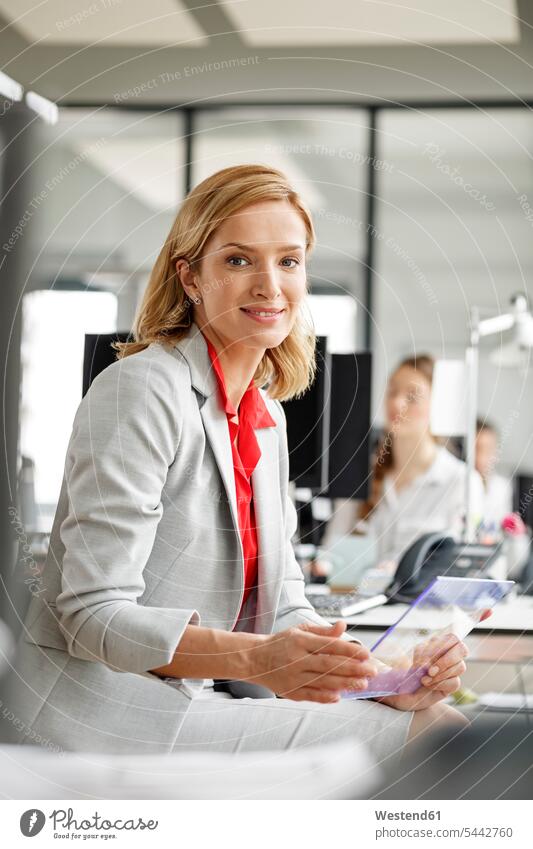 Portait of smiling businesswoman at desk in office holding futuristic tablet businesswomen business woman business women offices office room office rooms