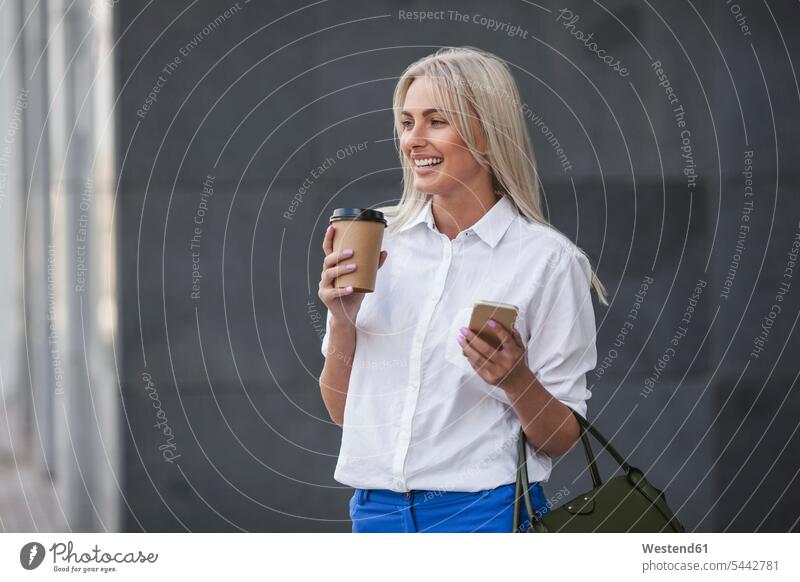 Happy businesswoman with takeaway coffee and cell phone outdoors businesswomen business woman business women females mobile phone mobiles mobile phones