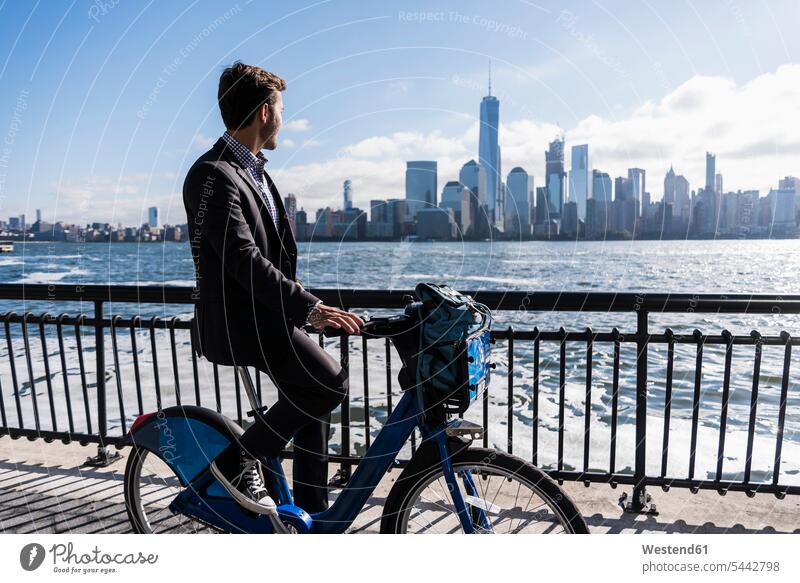 USA, man on bicycle at New Jersey waterfront with view to Manhattan bikes bicycles men males driving drive Businessman Business man Businessmen Business men