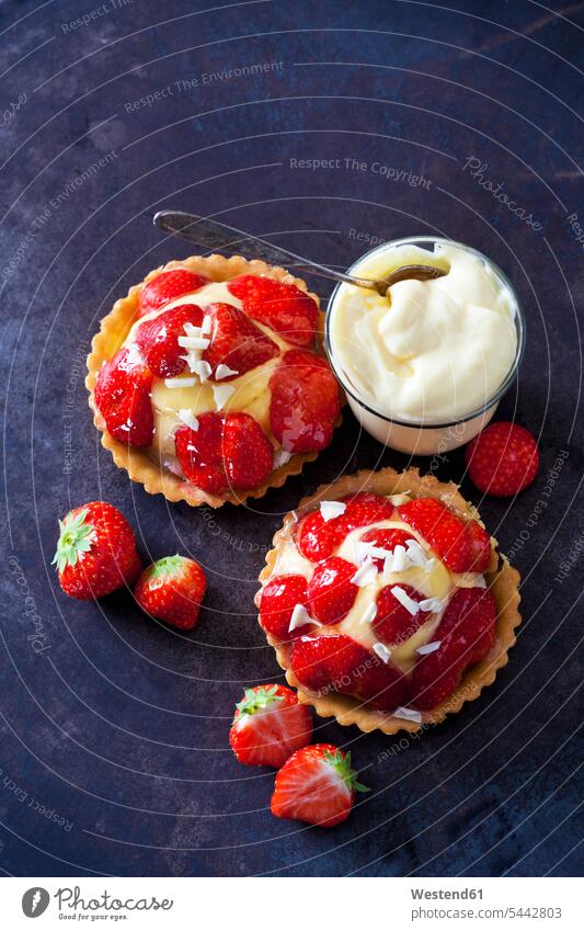 Two strawberry tartlets with custard and white chocolate shaving on dark ground Glass Glasses garnished ready to eat ready-to-eat short crust short pastry