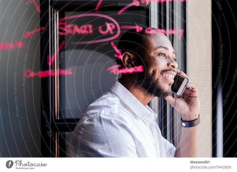 Smiling businessman on cell phone in office with writing on windowpane Businessman Business man Businessmen Business men window glass window glasses windowpanes