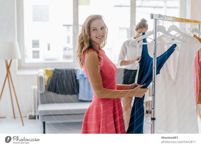 Smiling young woman choosing dress from clothes rail females women studio studios fashion fashionable Adults grown-ups grownups adult people persons human being