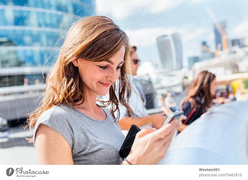 UK, London, smiling woman checking her smartphone females women mobile phone mobiles mobile phones Cellphone cell phone cell phones smile Adults grown-ups
