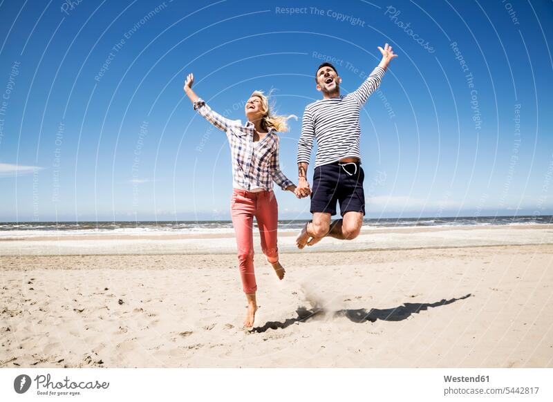 Happy carefree couple on the beach beaches twosomes partnership couples jumping Leaping Fun having fun funny laughing Laughter people persons human being humans