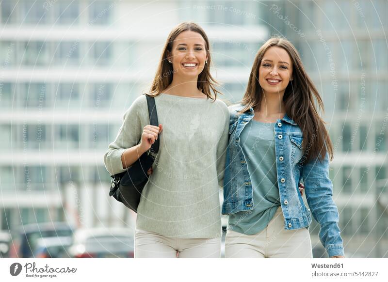 Two girlfriends walking in the city with arms around female friends laughing Laughter together happiness happy cheerful gaiety Joyous glad Cheerfulness