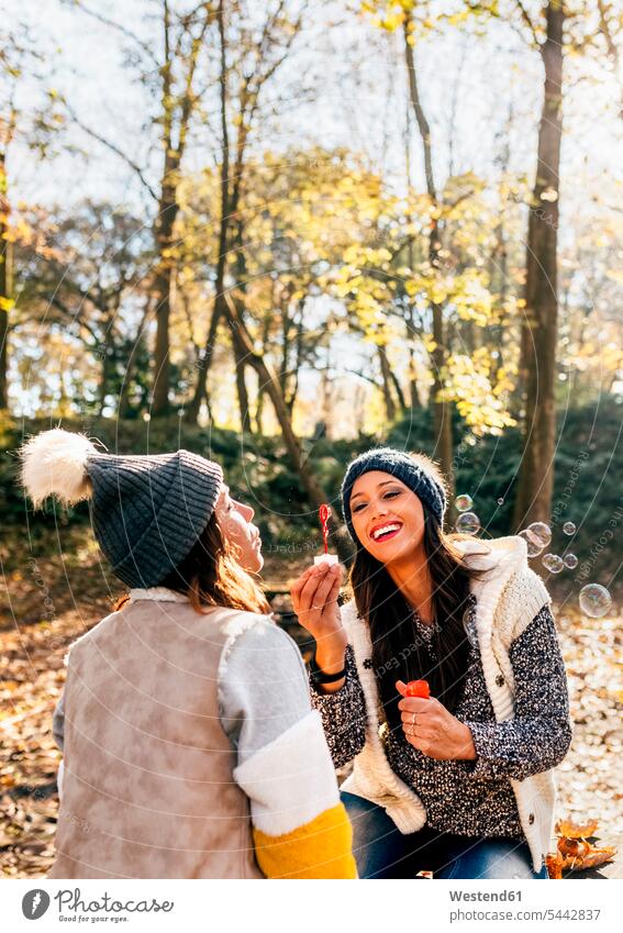 Two pretty women having fun with soap bubbles in an autumnal forest woman females female friends fall Fun funny beautiful woods forests Adults grown-ups