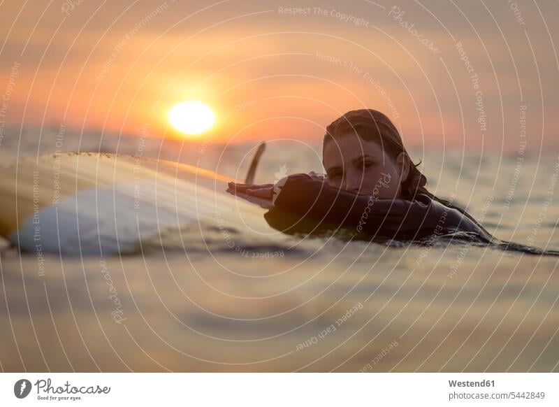 Indonesia, Bali, portrait of female surfer in the ocean at sunset surfing surf ride surf riding Surfboarding woman females women Sea water sports Water Sport
