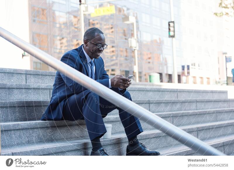 Smiling businessman sitting on stairs checking cell phone break mobile phone mobiles mobile phones Cellphone cell phones smiling smile Businessman Business man