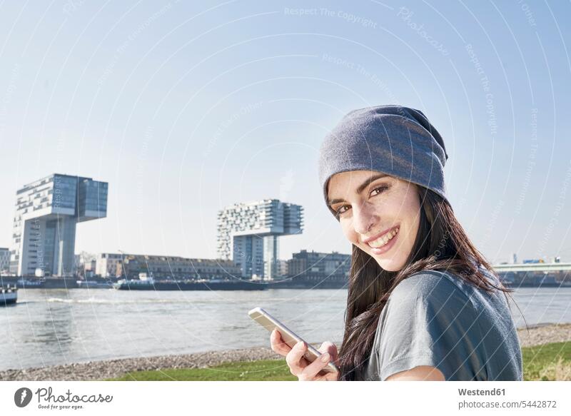 Germany, Cologne, portait of smiling young woman using cell phone at River Rhine smile females women mobile phone mobiles mobile phones Cellphone cell phones