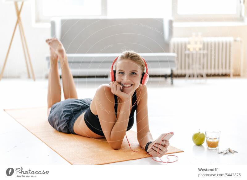 Smiling young woman in sportswear lying on gym mat listening to music laying down lie lying down mats Yoga mat gym mats Sportswear Activewear Sport Clothes