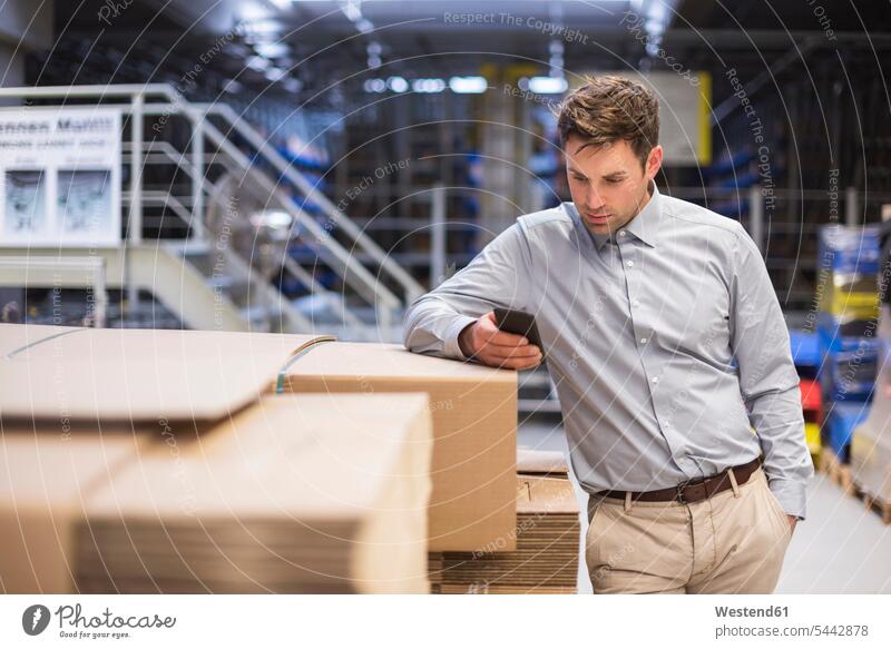 Man in factory looking at cell phone Businessman Business man Businessmen Business men males mobile phone mobiles mobile phones Cellphone cell phones storehouse
