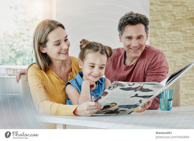 Happy family at home looking at picture book happiness happy eyeing daughter daughters reading books smiling smile families view seeing viewing child children