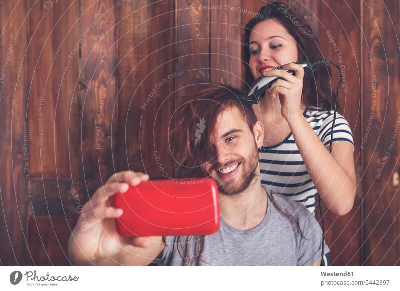Young man taking a selfie while getting a haircut by his girlfriend with hair cutting machine photographing Selfie Selfies couple twosomes partnership couples