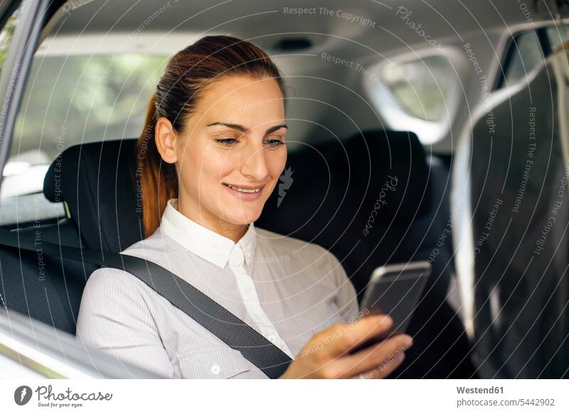 Businesswoman sitting on backseat of a car looking at cell phone businesswoman businesswomen business woman business women portrait portraits automobile Auto