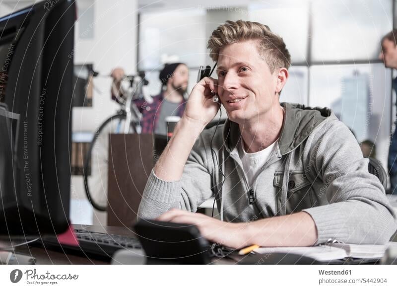 Young man at desk in office wearing a headset call center call centre call centres call centers headsets offices office room office rooms men males on the phone
