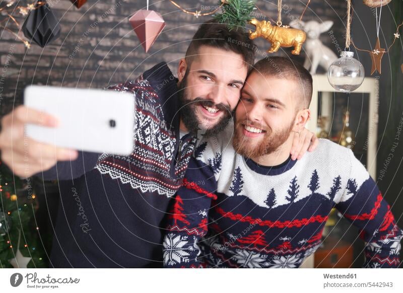 Portrait of happy gay couple taking selfie with smartphone at Christmas time at home Gay Couple Gays portrait portraits Selfie Selfies same-sex couple