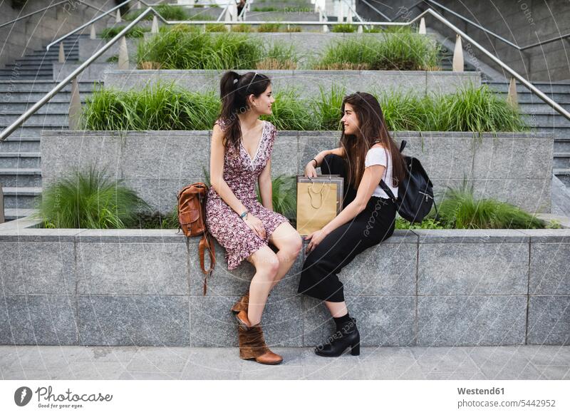Two young women sitting down and talking in the city smiling smile female friends speaking mate friendship woman females Adults grown-ups grownups adult people