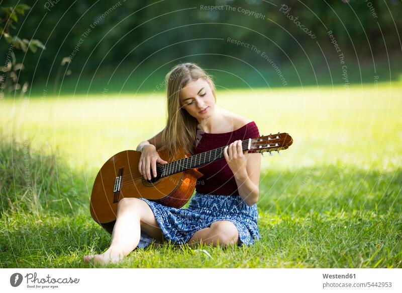 Young woman sitting on meadow, playing guitar Grass Grasses romantic lyrical Romance practicing practice practise exercise exercising practising learning
