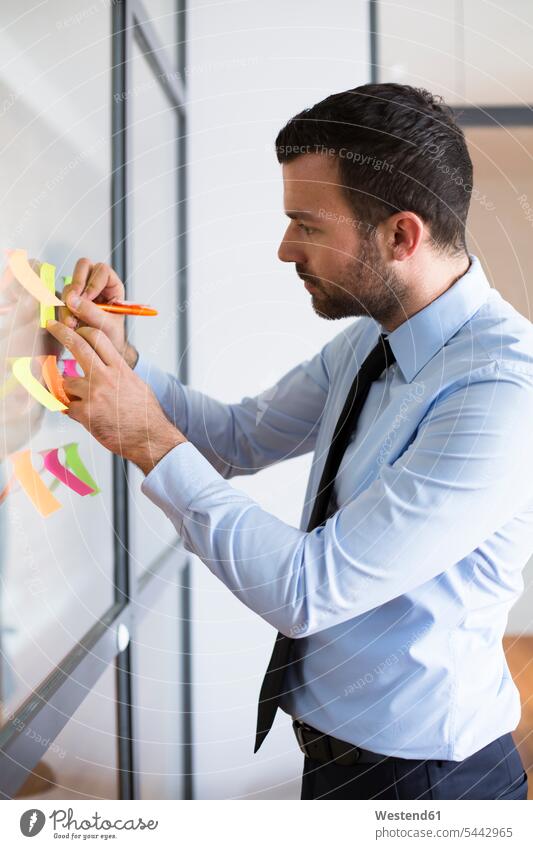 Businessman in office writing on adhesive note on glass wall Adhesive Note post-it note sticky notes adhesive notes Business man Businessmen Business men