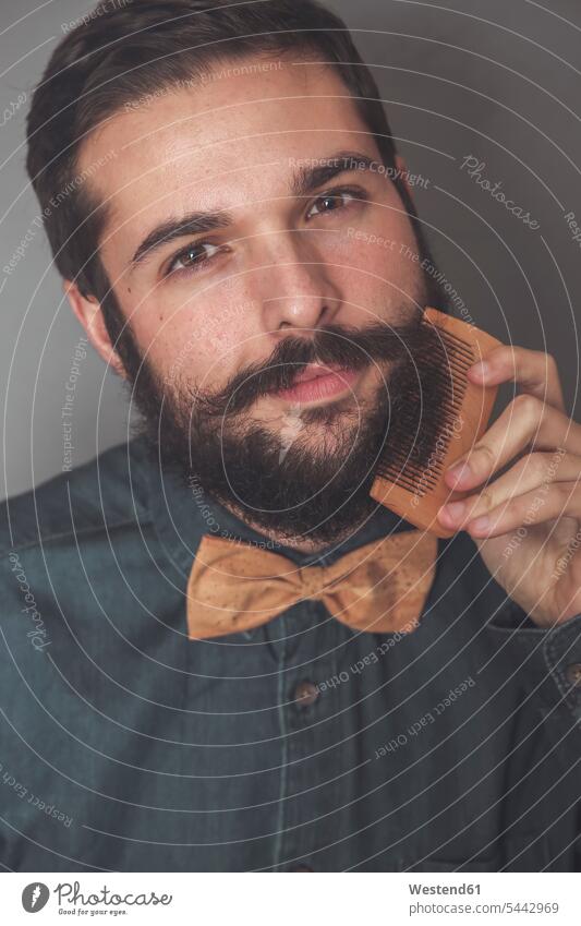 Man combing his beard with a wooden comb, wearing denim shirt and cork bow tie portrait portraits combs man men males people persons human being humans