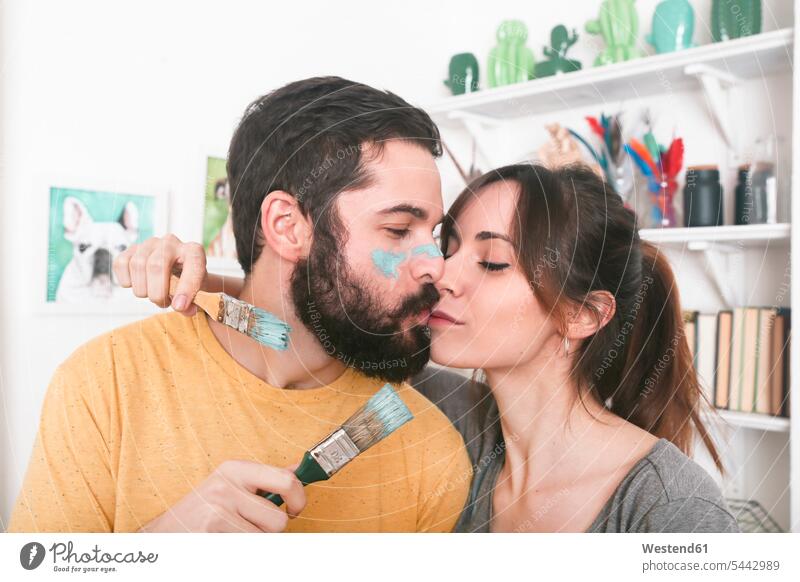 Young couple kissing holding paintbrushes twosomes partnership couples painting kisses people persons human being humans human beings indoors indoor shot