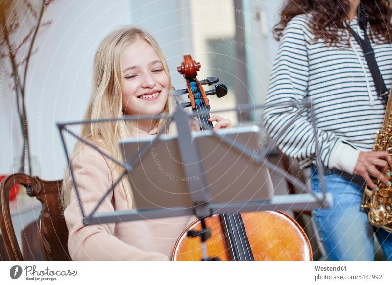 Two girls playing cello and saxophone together smiling smile females music child children kid kids people persons human being humans human beings