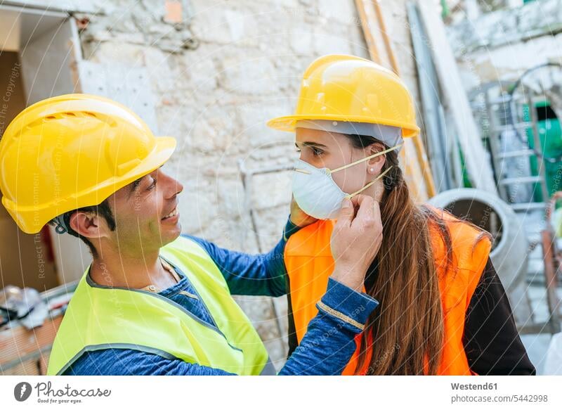 Man helping woman putting on dust mask on a construction site working At Work construction worker builders colleagues Building Site sites Building Sites