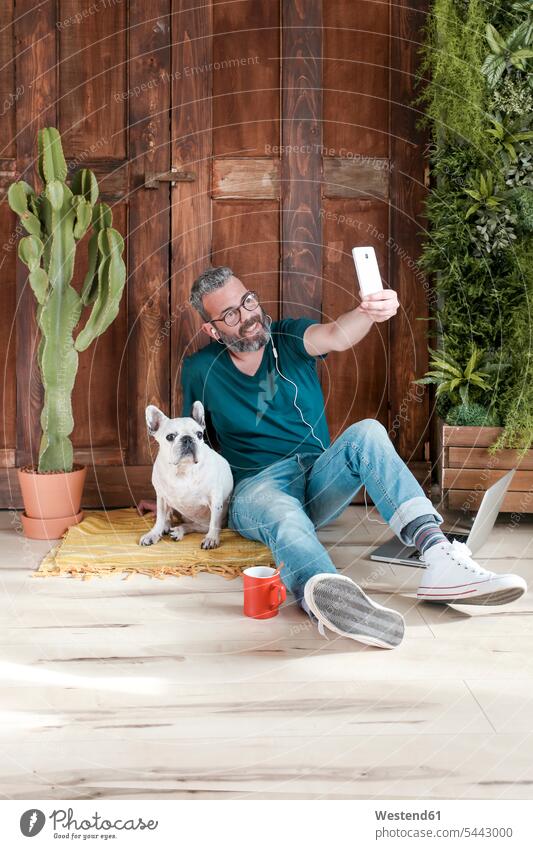 Bearded man sitting with his dog on the floor at home taking selfie with smartphone dogs Canine men males Selfie Selfies pets animal creatures animals Adults