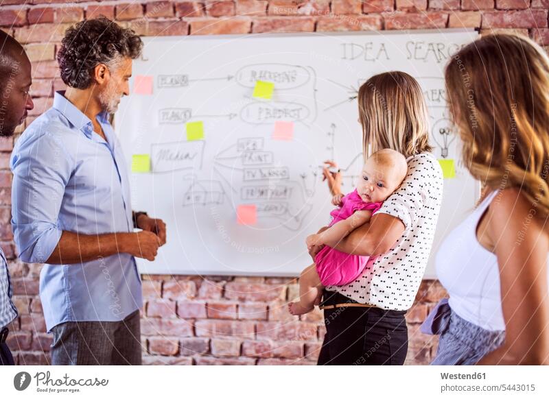 Mother with baby working together with team on whiteboard at brick wall in office infants nurselings babies mother mommy mothers ma mummy mama business