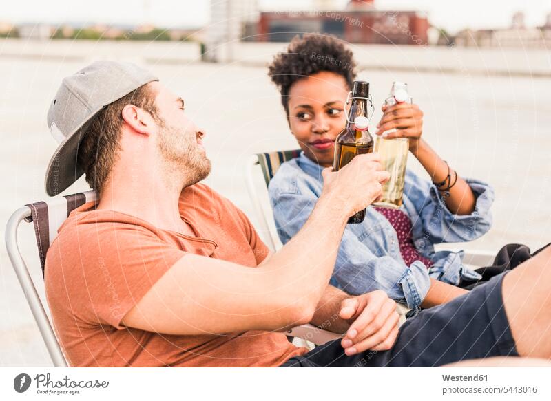 Young couple clinking beer bottles on rooftop Party Parties relaxed relaxation twosomes partnership couples Beer Beers Ale drinking toasting cheers roof terrace
