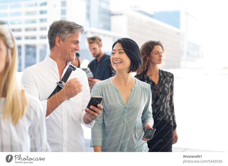 Group of casual businesspeople socializing on urban square colleagues smiling smile mobile phone mobiles mobile phones Cellphone cell phone cell phones