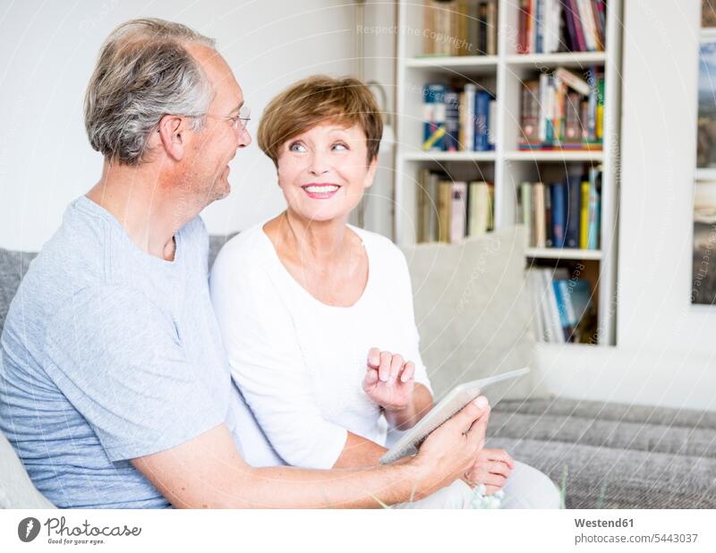 Senior couple at home sitting on couch using digital tablet settee sofa sofas couches settees Seated smiling smile twosomes partnership couples relaxed