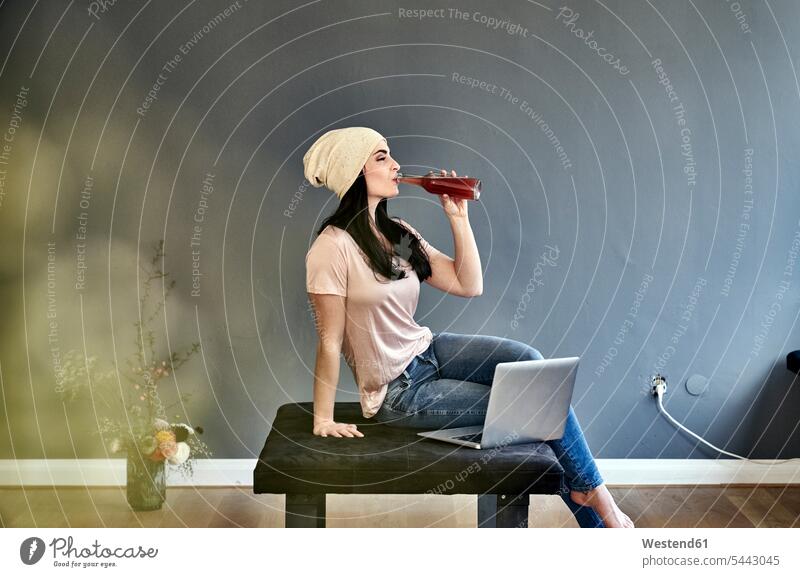 Young woman with laptop drinking from bottle sitting Seated Bottle Bottles females women Laptop Computers laptops notebook Adults grown-ups grownups adult