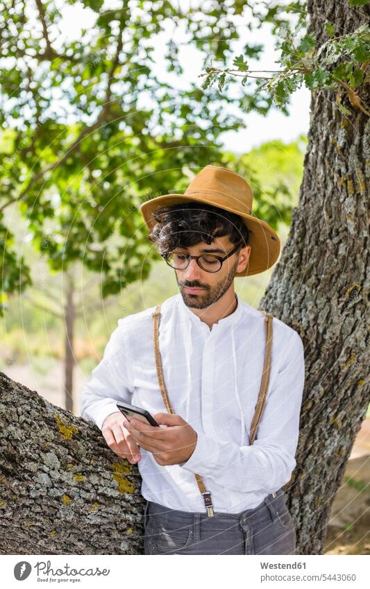 Man wearing old-fashioned clothes using cell phone man men males mobile phone mobiles mobile phones Cellphone cell phones Tree Trees Adults grown-ups grownups