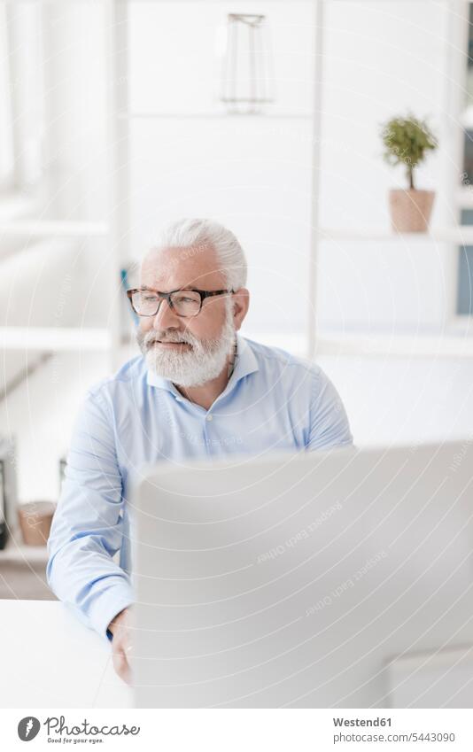 Smiling mature man with beard and glasses at desk smiling smile men males Adults grown-ups grownups adult people persons human being humans human beings