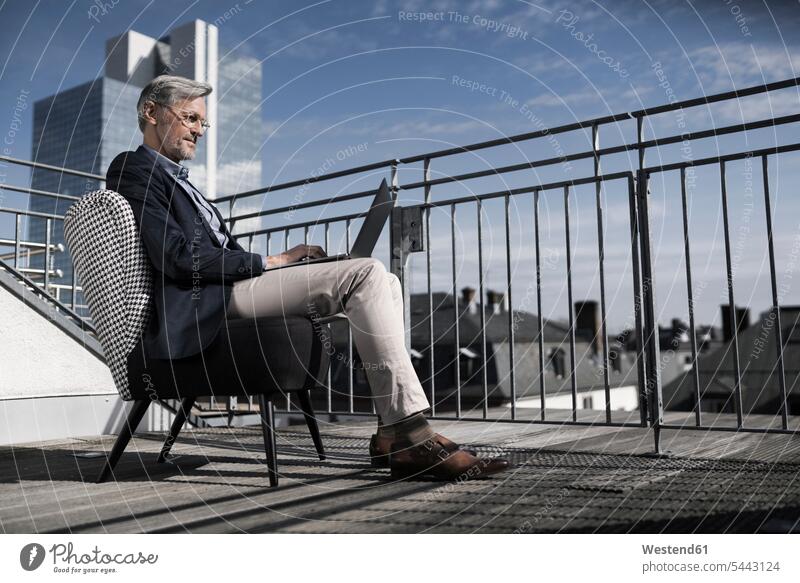 Grey-haired businessman sitting on balcony using laptop Laptop Computers laptops notebook Businessman Business man Businessmen Business men Seated computer