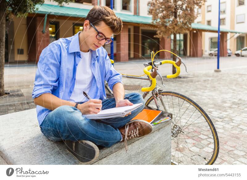 Young man with racing cycle sitting on bench writing on notepad student students learning write education Seated bicycle bikes bicycles men males