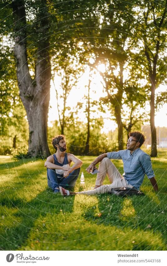 Two friends sitting in a park with mobile device and papers Seated mobile phone mobiles mobile phones Cellphone cell phone cell phones parks man men males