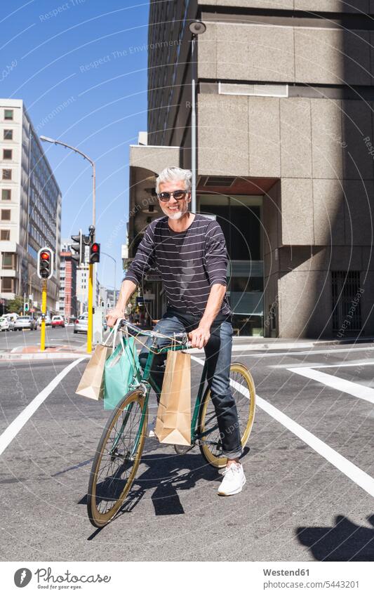 Mature man riding bicycle in the city bikes bicycles smiling smile shopping bag shopping-bag shopping-bags shopping bags on the move on the way on the go
