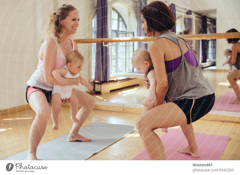 Two mothers working out on yoga mats with babies in their arms mommy mummy mama exercising exercise training practising smiling smile baby infants nurselings