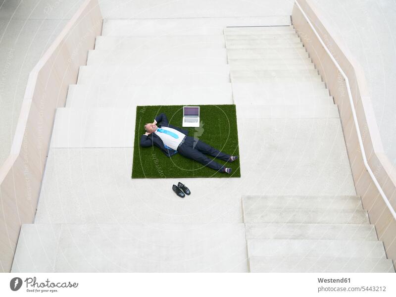 Top view of businesssman lying on stairs next to laptop laying down lie lying down stairway Laptop Computers laptops notebook Businessman Business man