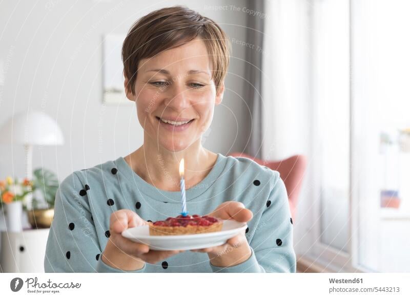 Portrait of smiling woman holding plate with birthday cake portrait portraits Birthday cake Birthday cakes females women fancy cake Torte pies Sweet Food sweet